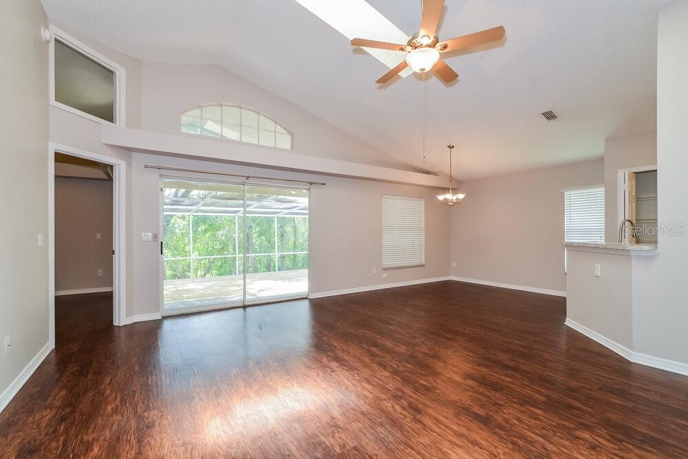 An empty living room features dark wood-look flooring, a vaulted ceiling, and sliding glass doors — 996 MAPLE COURT, APOPKA, FL