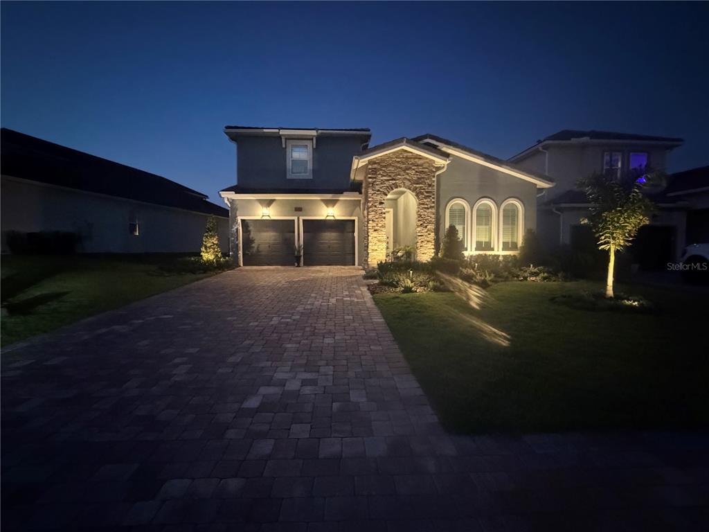 A two-story house with a stone-accented entryway, arched windows, and a paved driveway at dusk — 16136 VOLTERRA POINT, BELLA COLLINA, FL