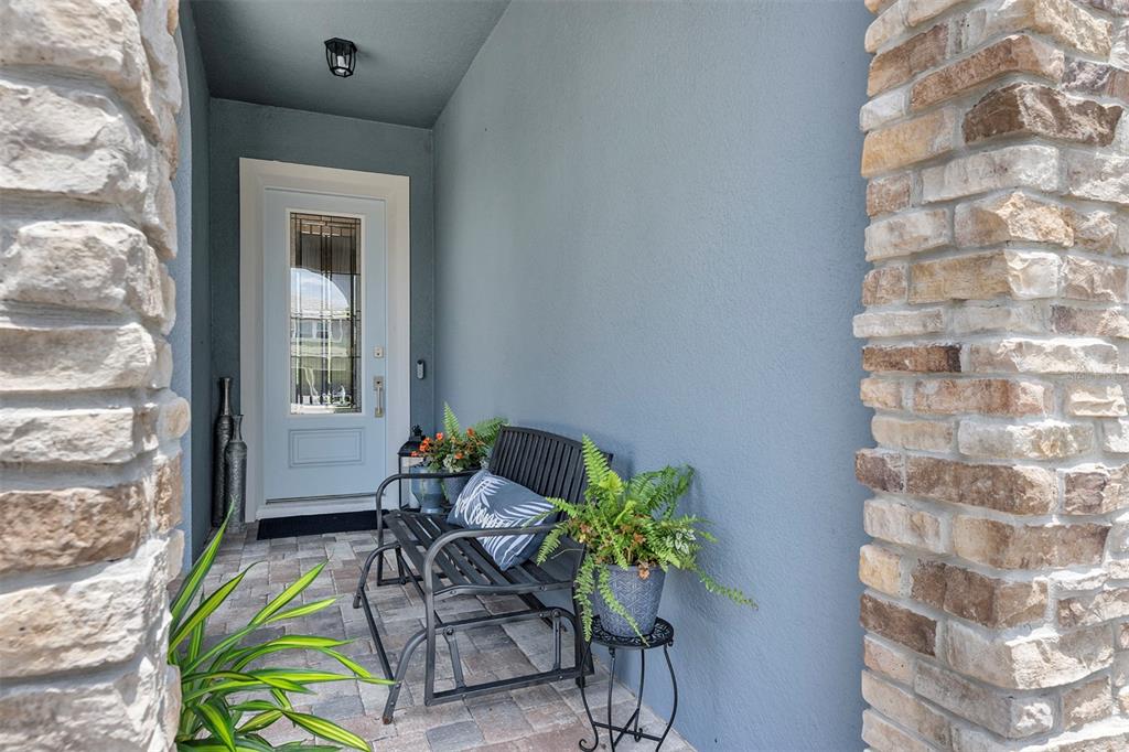 A covered entryway features a light blue door, stone pillars, and a black metal bench — 16136 VOLTERRA POINT, BELLA COLLINA, FL