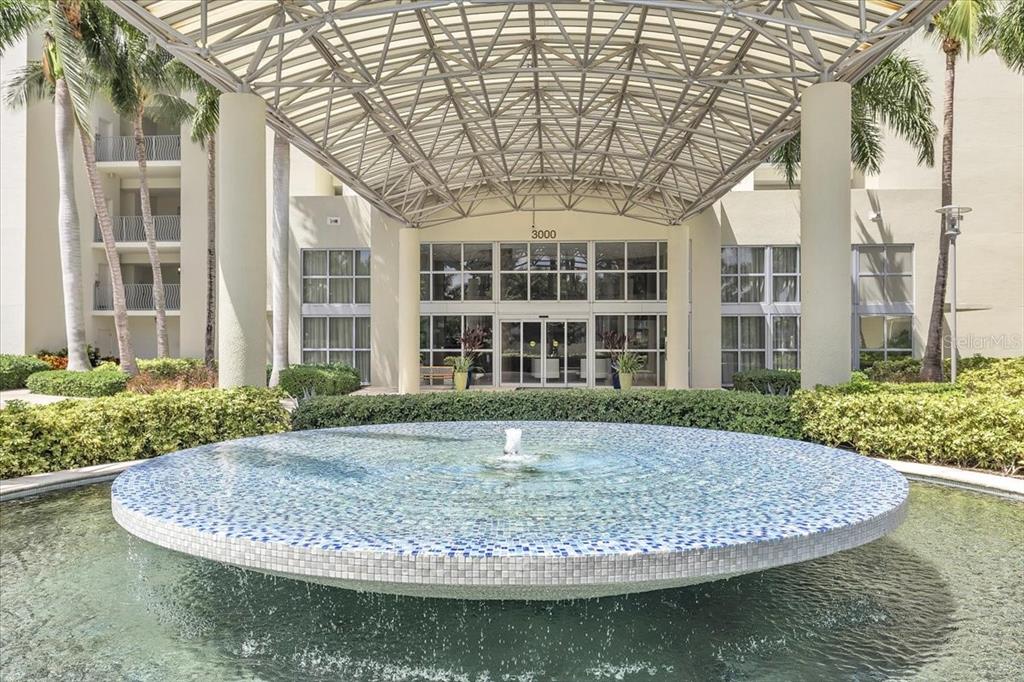 A circular fountain sits in front of a building entrance with a large metal canopy — 3000 OASIS GRAND BOULEVARD UNIT 2802, FORT MYERS, FL