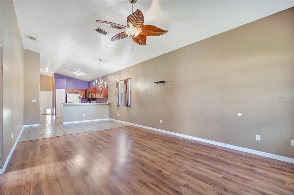 A living room with wood-look flooring, a ceiling fan, and an open kitchen beyond — 135 PARKER COVE COURT, OCOEE, FL