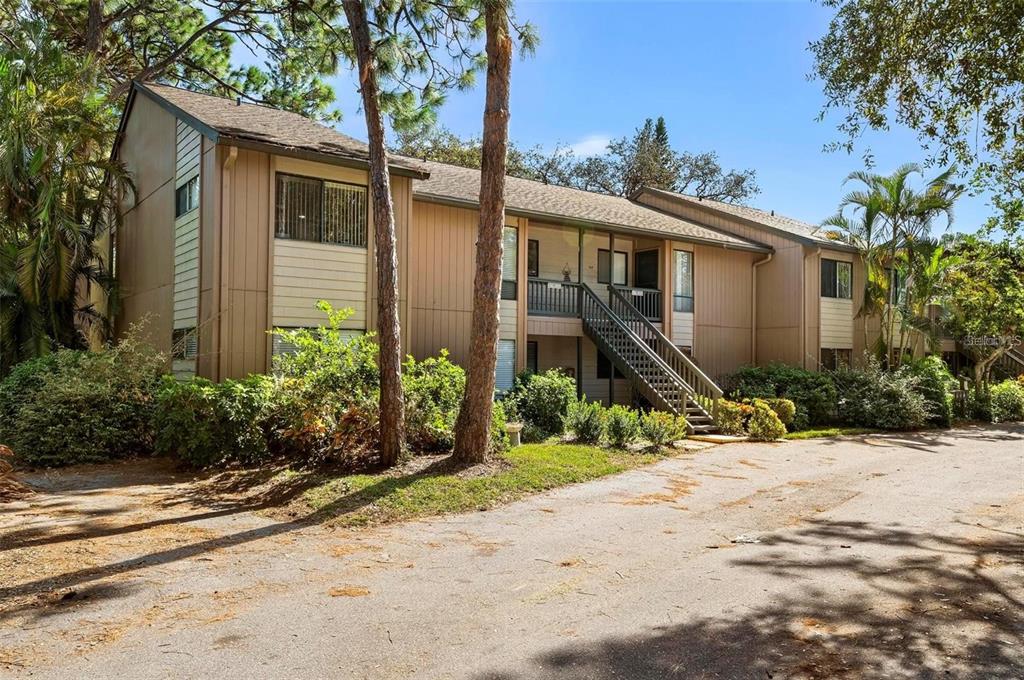 A two-story tan apartment building with an exterior staircase and surrounding trees — 1707 PELICAN COVE ROAD UNIT 451, SARASOTA, FL