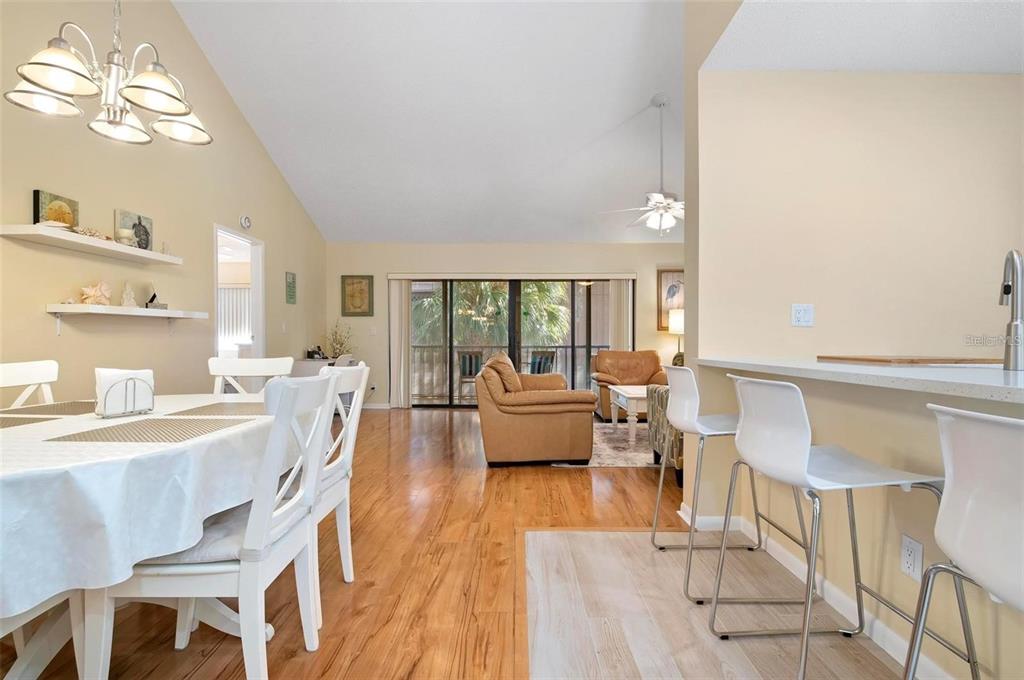 A dining area and kitchen breakfast bar overlook a living room with sliding glass doors — 1707 PELICAN COVE ROAD UNIT 451, SARASOTA, FL