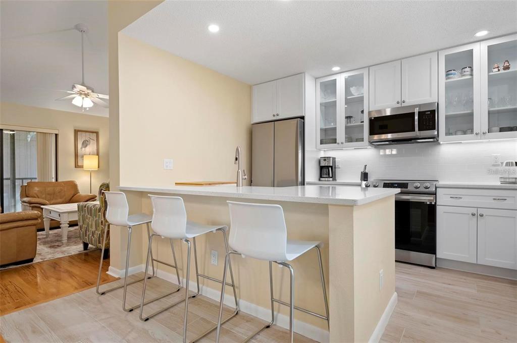 A kitchen with white cabinets, stainless steel appliances, and a breakfast bar with three stools — 1707 PELICAN COVE ROAD UNIT 451, SARASOTA, FL