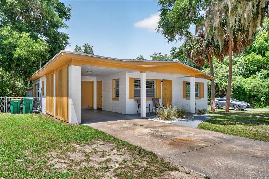 A single-story house with a carport, white block walls, and yellow trim under trees — 529 E GOTTSCHE AVENUE, EUSTIS, FL