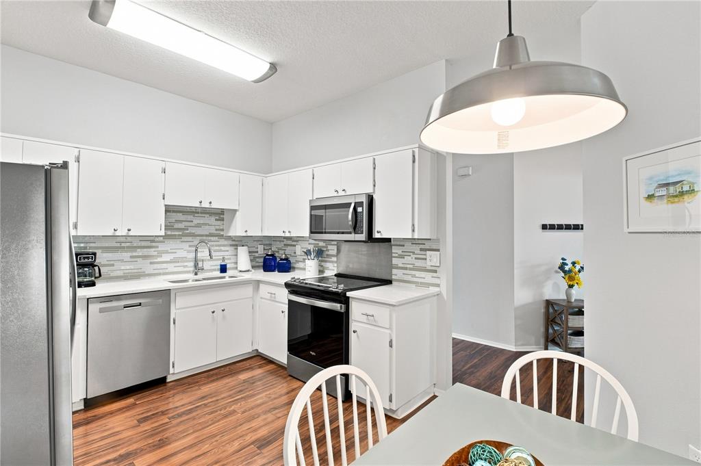 A kitchen features white cabinets, stainless steel appliances, a tiled backsplash, and wood-look flooring — 864 FRANKLIN CIRCLE, PALM HARBOR, FL