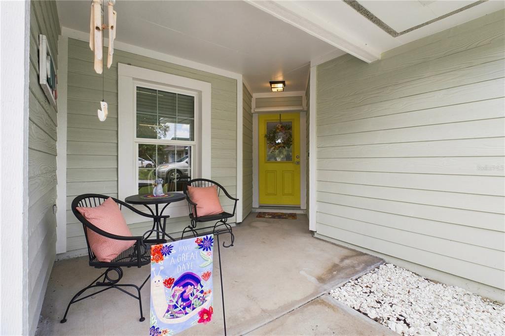A covered front porch features light green siding, a yellow door, and two black chairs — 864 FRANKLIN CIRCLE, PALM HARBOR, FL