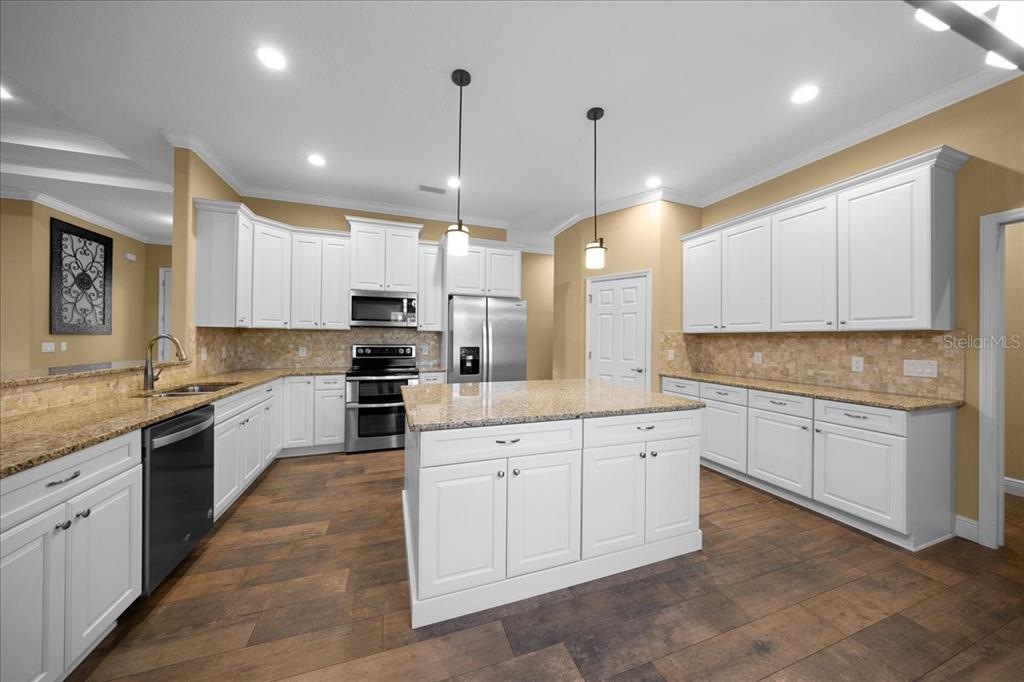 A kitchen features white cabinets, granite countertops, a center island, and wood-look flooring — 2087 N ANNAPOLIS AVENUE, HERNANDO, FL