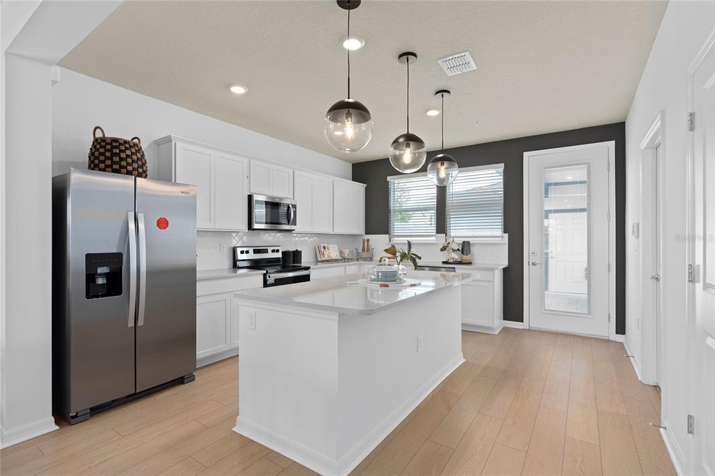 A modern kitchen features white cabinetry, a central island, stainless steel appliances, and wood flooring — 10506 EVENING STAR STREET, ORLANDO, FL
