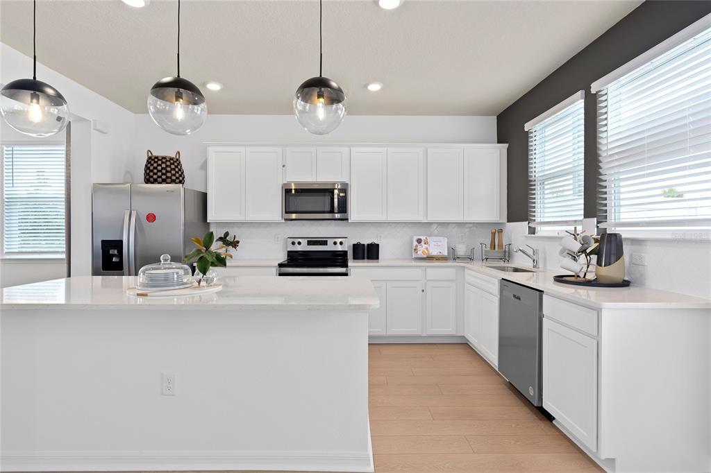 A modern kitchen features white cabinetry, stainless steel appliances, a large island, and pendant lighting — 10506 EVENING STAR STREET, ORLANDO, FL