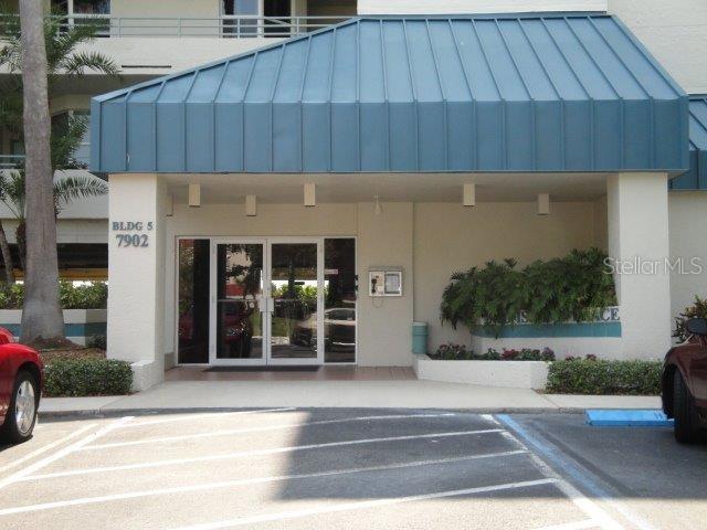 The exterior entrance of a multi-story building features a blue metal awning and glass doors — 7902 SAILBOAT KEY BOULEVARD S UNIT 402, SOUTH PASADENA, FL