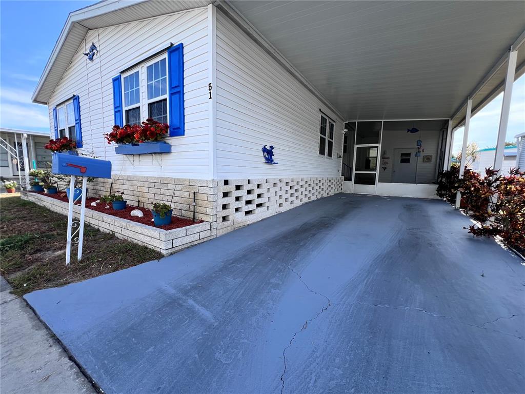 A white mobile home features blue shutters, a carport, and a brick-patterned foundation — 51 PINDO PALM STREET E, LARGO, FL