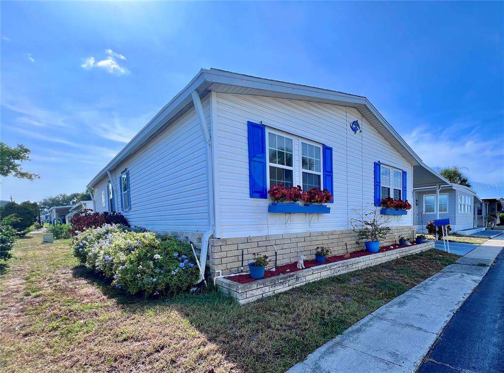 A white manufactured home with blue shutters and a brick planter bed in the front — 51 PINDO PALM STREET E, LARGO, FL