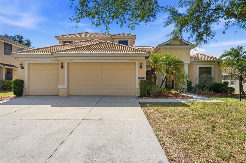 A two-story house with a three-car garage and a tiled roof under a blue sky — 6611 CHICKADEE LANE, BRADENTON, FL