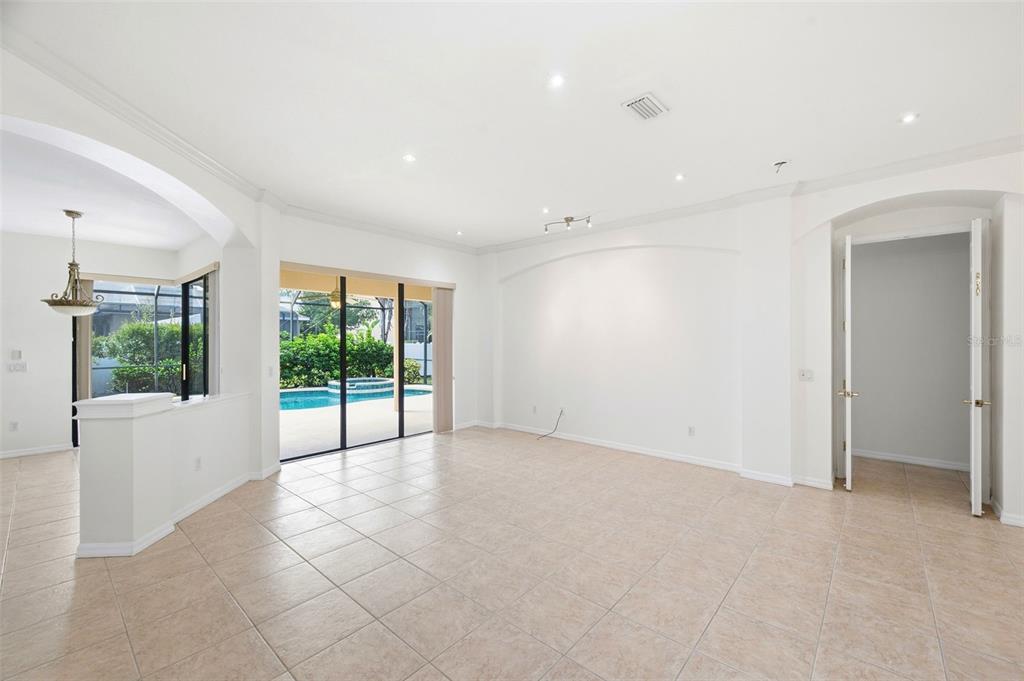 A bright living room with tile floors, recessed lighting, and sliding doors opening to a pool — 6611 CHICKADEE LANE, BRADENTON, FL