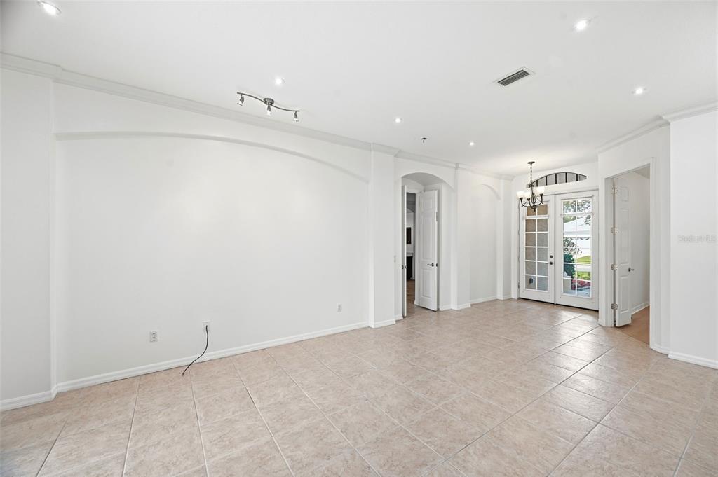 A bright, empty room with white walls, tile flooring, recessed lighting, and glass French doors — 6611 CHICKADEE LANE, BRADENTON, FL