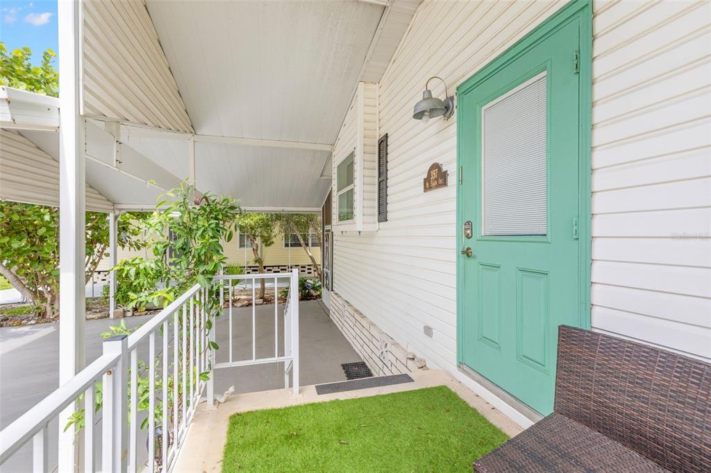 A covered porch features a teal door, white siding, a white railing, and artificial grass — 357 MOUNT SAXON AVENUE NE UNIT 323, ST PETERSBURG, FL