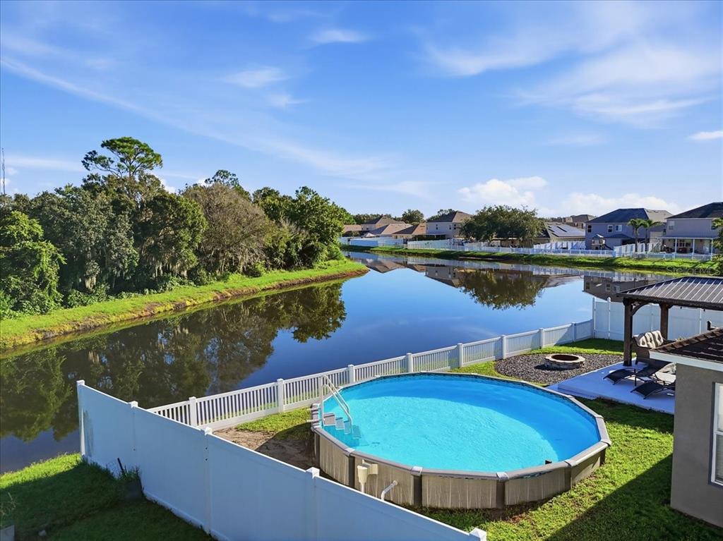 An above-ground swimming pool sits in a fenced backyard overlooking a calm lake — 3116 KEARNS ROAD, MULBERRY, FL