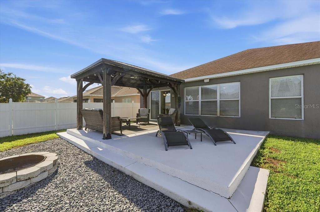 A backyard patio features a wooden pergola, outdoor furniture, lounge chairs, and a fire pit — 3116 KEARNS ROAD, MULBERRY, FL