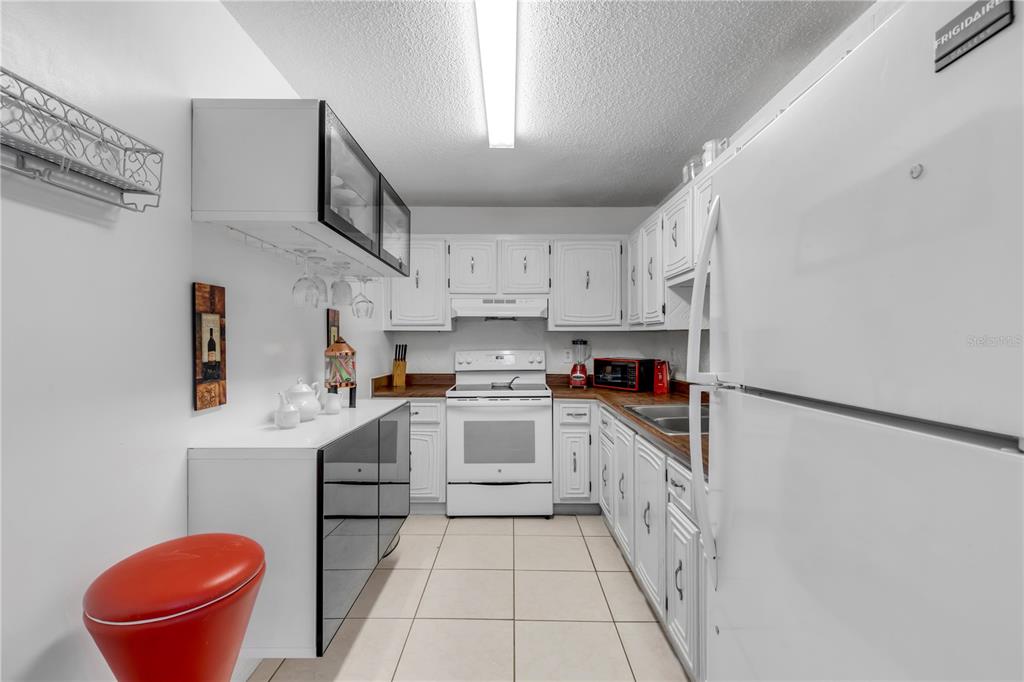 A galley kitchen features white cabinets, white appliances, dark countertops, and light tile flooring — 2711 N HALIFAX AVENUE UNIT 372, DAYTONA BEACH, FL