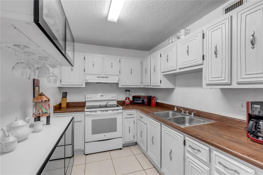 A kitchen with white cabinets, wood countertops, a white stove, and a double basin sink — 2711 N HALIFAX AVENUE UNIT 372, DAYTONA BEACH, FL