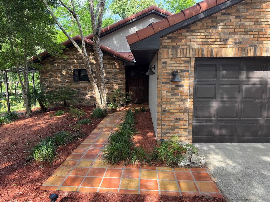 A brick house exterior features a tiled walkway leading to a recessed front door — 39 FOREST LANE, EUSTIS, FL
