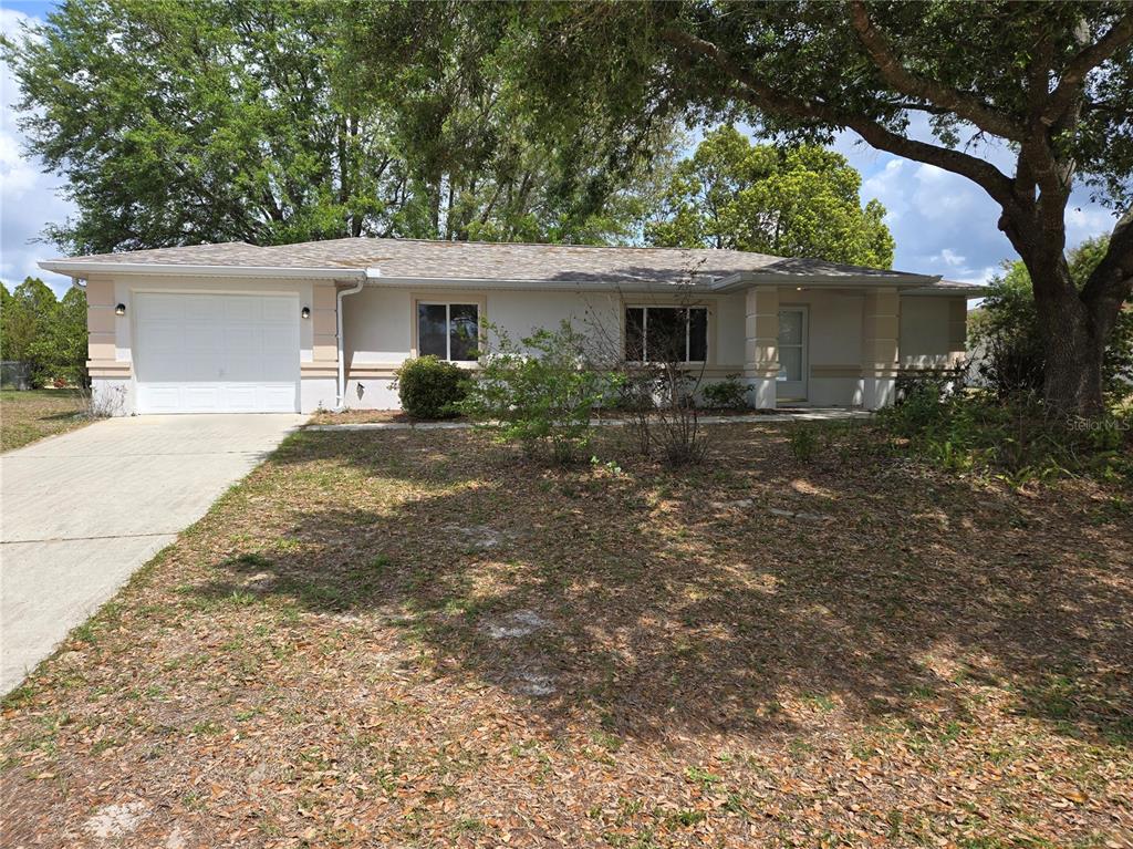 A single-story house with a white garage, beige trim, and a large tree in front — 6121 SW 103RD LOOP, OCALA, FL