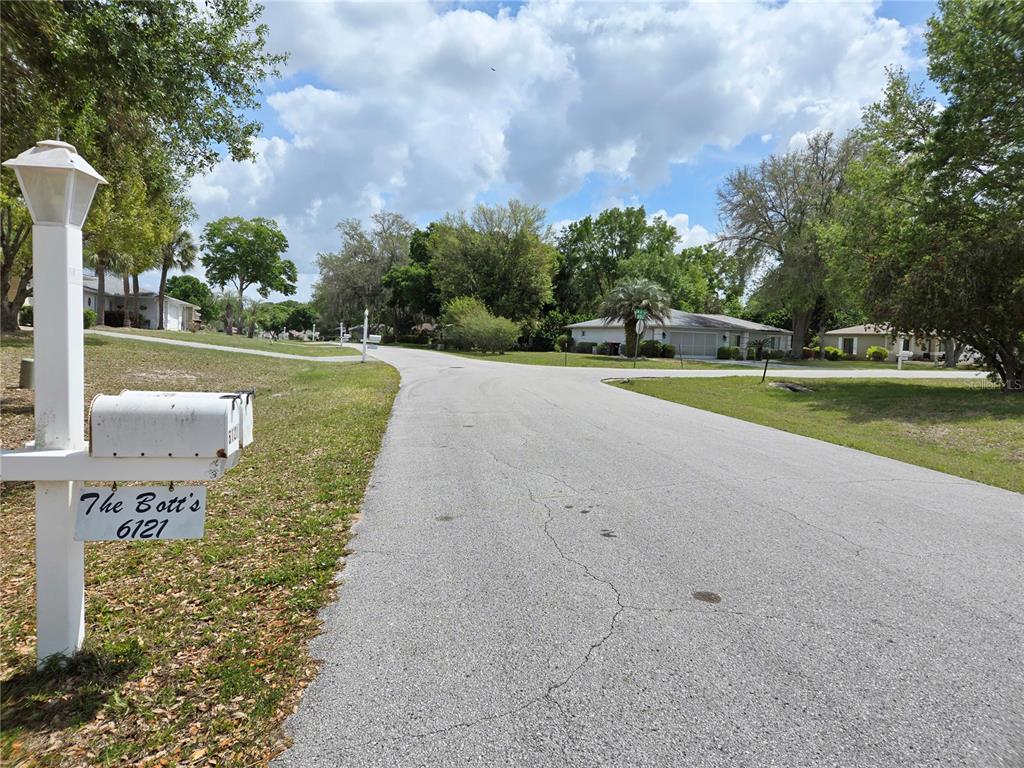 A mailbox stands on a post beside a paved residential street with trees and houses — 6121 SW 103RD LOOP, OCALA, FL