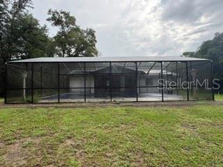 A screened-in pool enclosure sits behind a house with a grassy lawn in the foreground — 19279 SW 96TH LOOP, DUNNELLON, FL