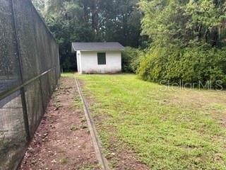 A small white shed stands in a grassy backyard next to a tall mesh fence — 19279 SW 96TH LOOP, DUNNELLON, FL