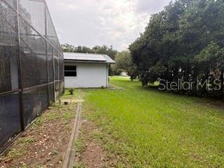 A view of a grassy backyard next to a house with a screened-in pool enclosure — 19279 SW 96TH LOOP, DUNNELLON, FL