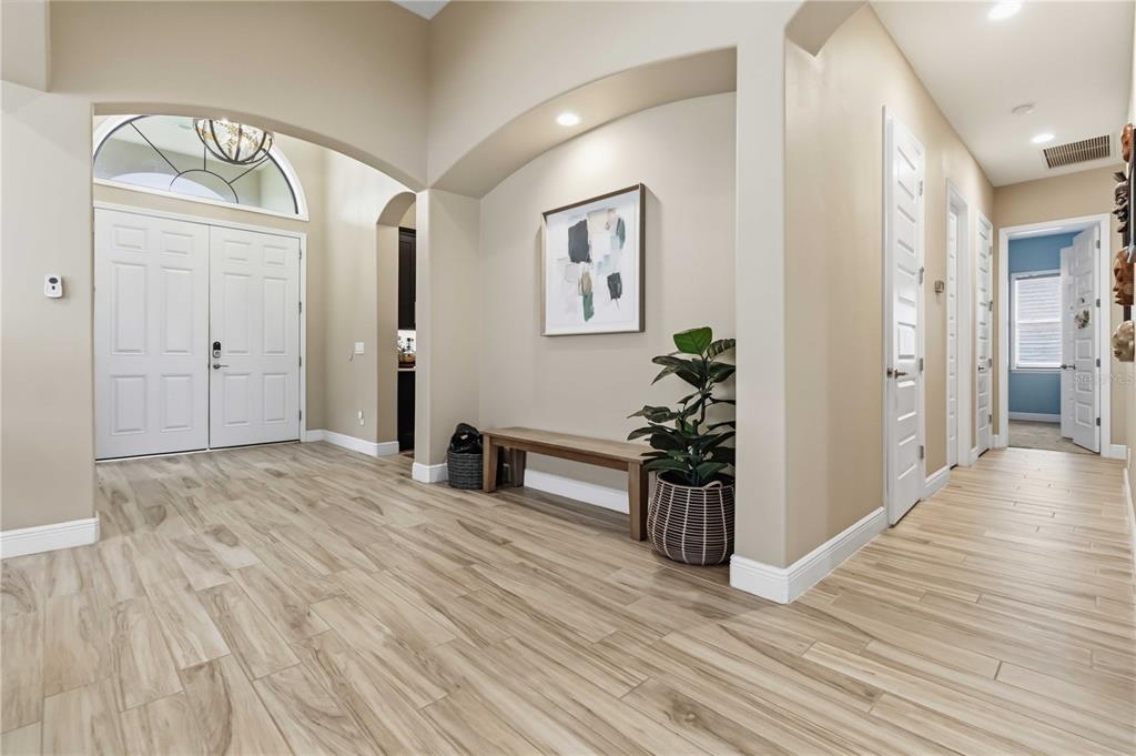 A bright entryway features light wood-look tile flooring, a wooden bench, and a white double door — 7966 WYNDHAM DRIVE, MELBOURNE, FL