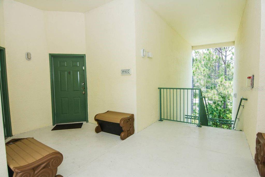 An outdoor apartment entryway features a green door, a small bench, and a metal railing — 8923 LEGACY COURT UNIT 302, KISSIMMEE, FL