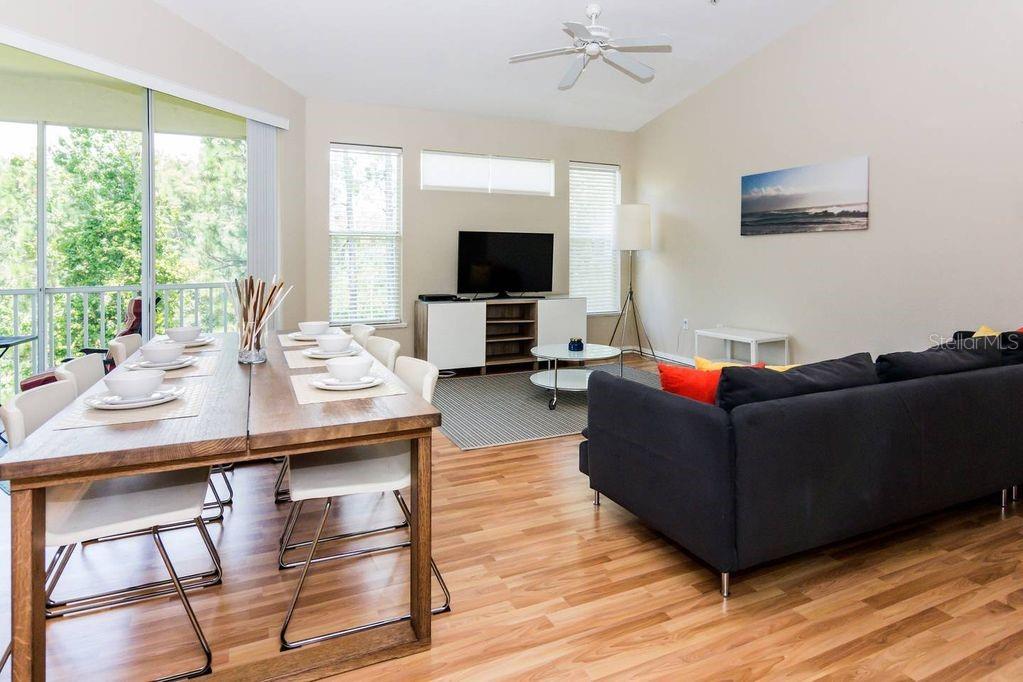 A living and dining area with wood flooring, a dark sofa, and a dining table — 8923 LEGACY COURT UNIT 302, KISSIMMEE, FL