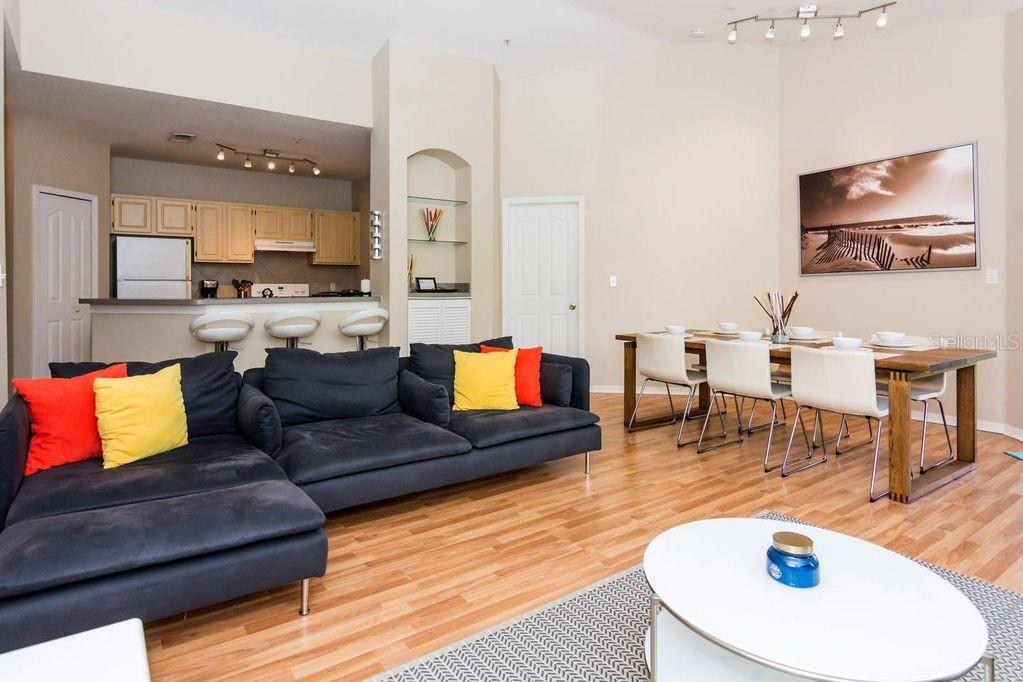 An open-concept living and dining area features a dark sectional sofa, wood flooring, and kitchen — 8923 LEGACY COURT UNIT 302, KISSIMMEE, FL
