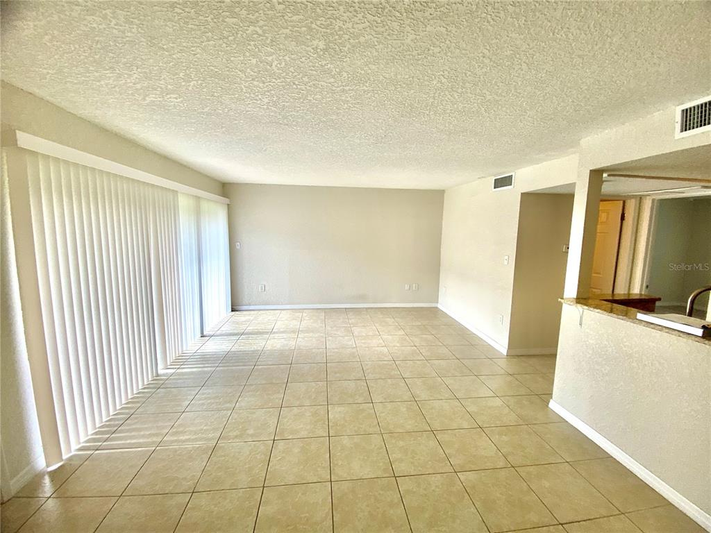 An empty living room with light-colored tile flooring, beige walls, and vertical blinds — 554 ORANGE DRIVE UNIT 15, ALTAMONTE SPRINGS, FL