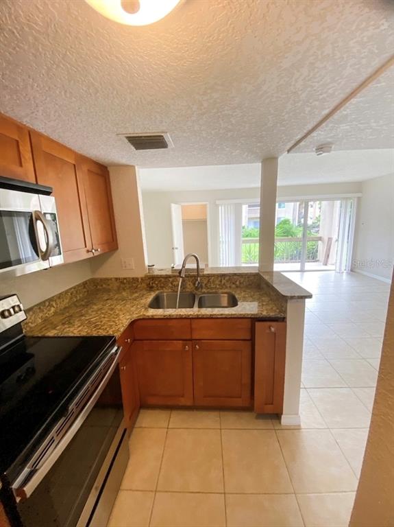 A kitchen with wood cabinets, granite countertops, and a stainless steel microwave overlooks a living area — 554 ORANGE DRIVE UNIT 15, ALTAMONTE SPRINGS, FL