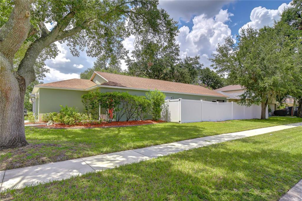 A single-story house with green siding and a white vinyl fence sits behind a sidewalk — 8736 MORRISON OAKS COURT, TEMPLE TERRACE, FL