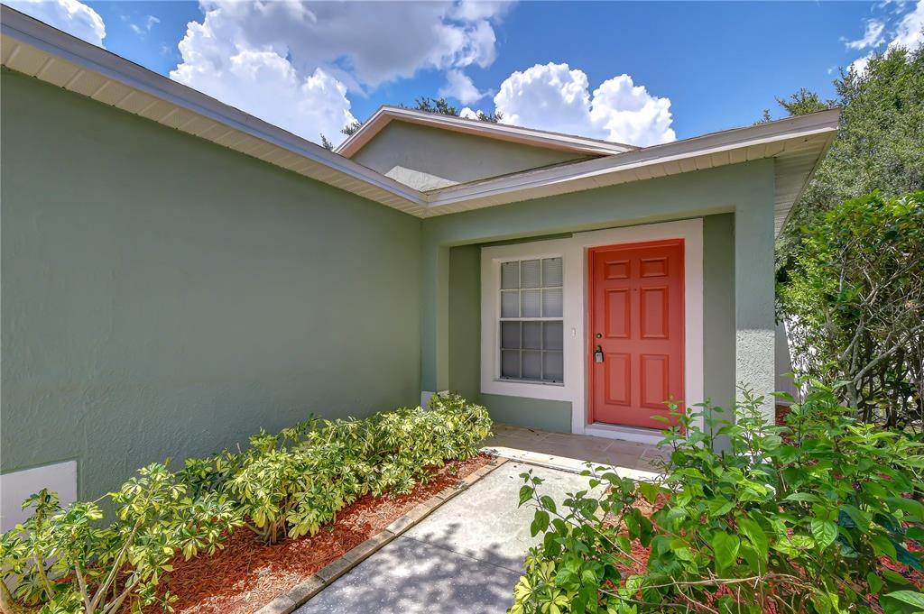 A green stucco house exterior features a red front door and a concrete walkway — 8736 MORRISON OAKS COURT, TEMPLE TERRACE, FL