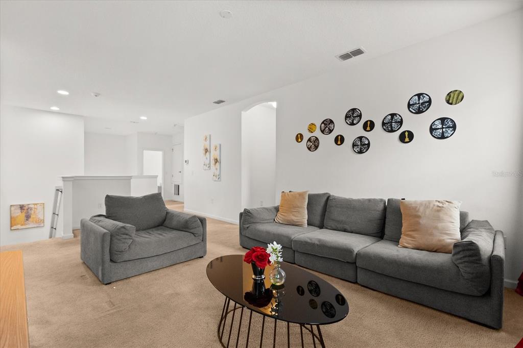 A carpeted living room features a gray sofa, matching armchair, and a black oval coffee table — 4565 CABELLO LOOP, KISSIMMEE, FL