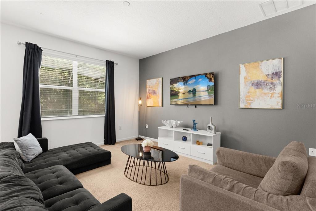 A living room features a grey accent wall, a mounted television, and neutral carpeting — 4565 CABELLO LOOP, KISSIMMEE, FL