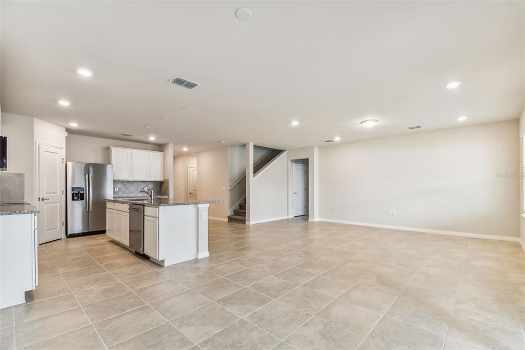 An open-concept kitchen and living area featuring tile flooring, white cabinetry, and stainless steel appliances — 6586 ASBURY BARNES STREET, WESLEY CHAPEL, FL