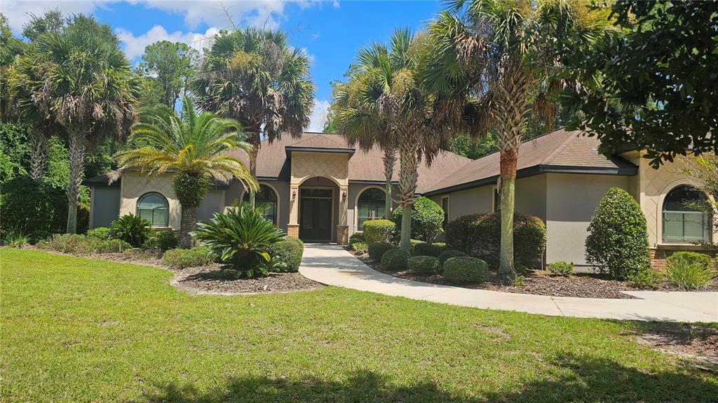 A single-story house with a tan stucco exterior, arched windows, and palm trees in the yard — 6019 NW 90TH STREET, GAINESVILLE, FL