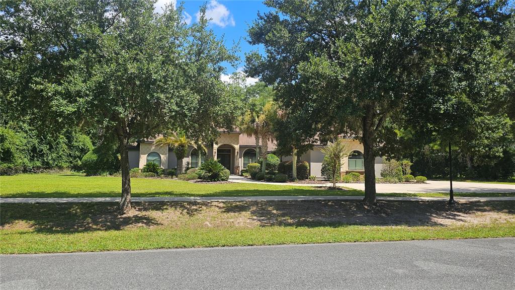 A single-story house with a beige stucco exterior sits behind a large lawn and trees — 6019 NW 90TH STREET, GAINESVILLE, FL