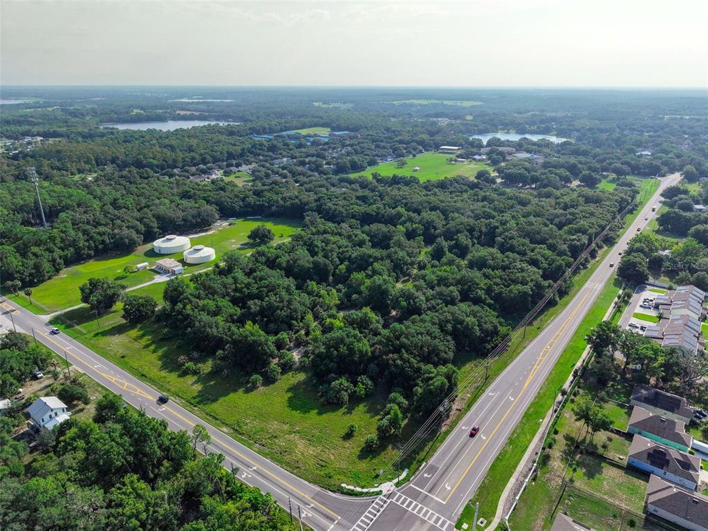 An aerial view shows a wooded lot bordered by two roads and nearby residential houses — E COUNTY ROAD 44, EUSTIS, FL