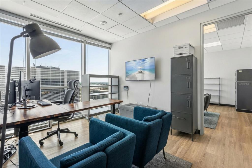 A modern office features a wooden desk, blue armchairs, a wall-mounted television, and city views — 189 S ORANGE AVENUE UNIT 1930S, ORLANDO, FL