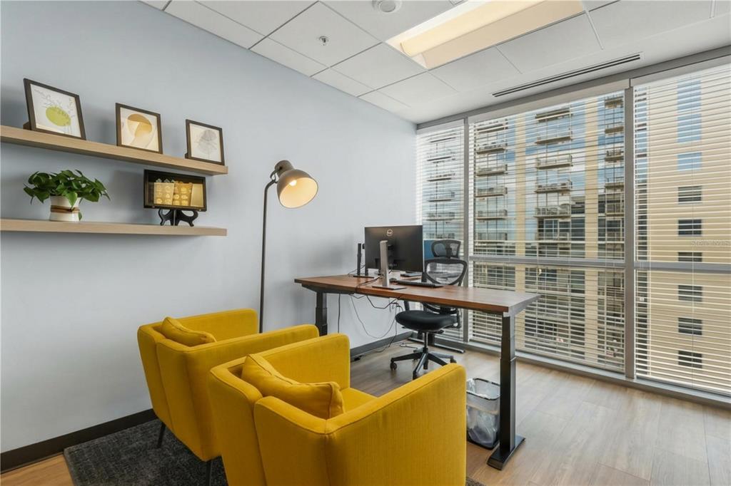 A home office features two yellow armchairs, a standing desk, floating shelves, and floor-to-ceiling windows — 189 S ORANGE AVENUE UNIT 1930S, ORLANDO, FL