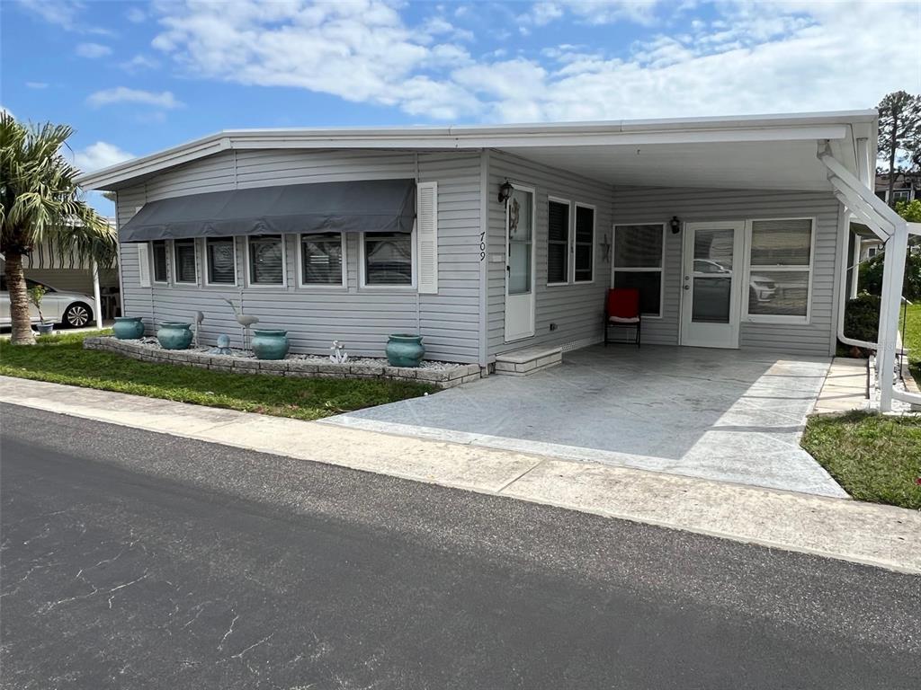 A light gray manufactured home features a carport, a front awning, and a small garden bed — 709 SUGAR PALM STREET, LARGO, FL