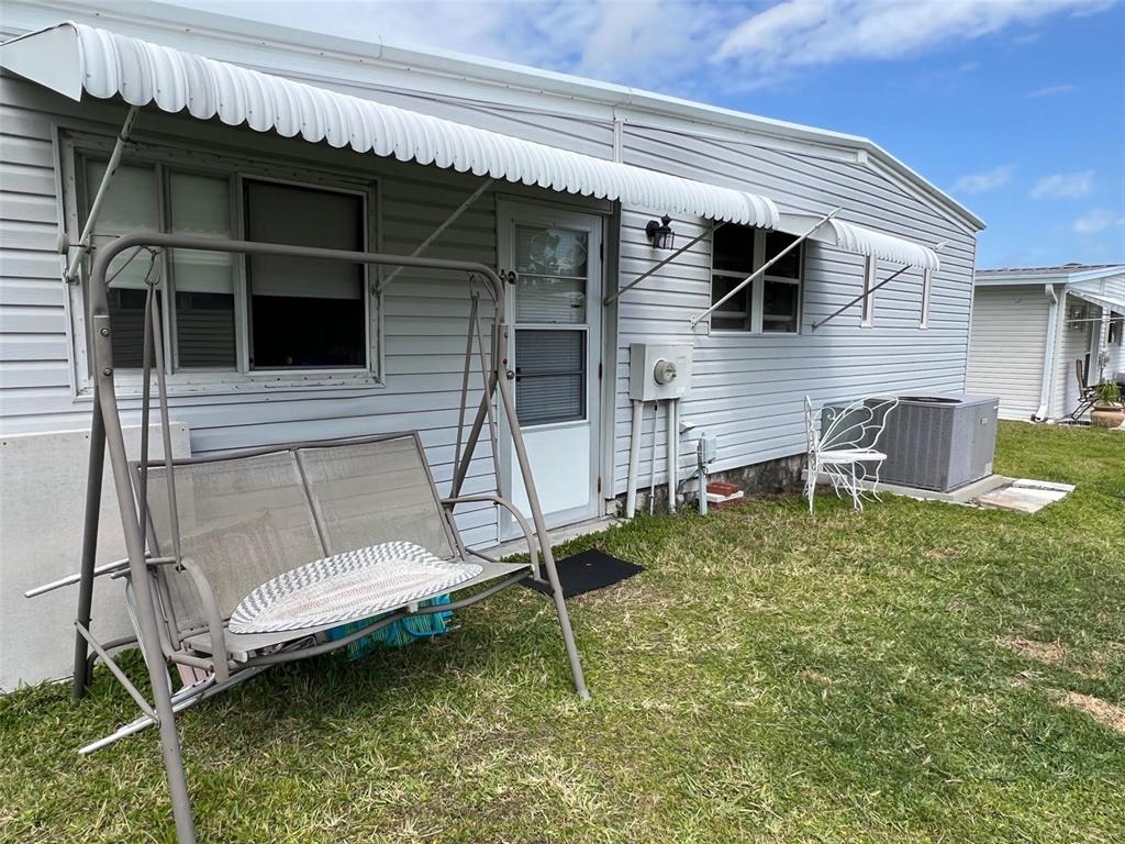 A light-colored mobile home exterior features a metal porch swing and a central door — 709 SUGAR PALM STREET, LARGO, FL