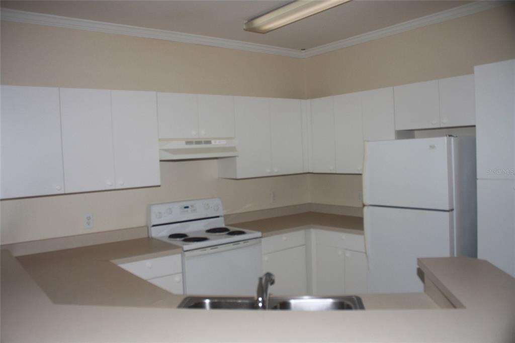A kitchen with white cabinets, white appliances, and tan countertops features a double-basin sink — 3561 CONROY ROAD UNIT 234, ORLANDO, FL